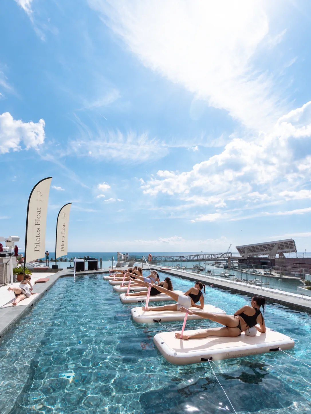 Guests mid-class on Pilates Float boards in a rooftop pool under a wide blue sky
